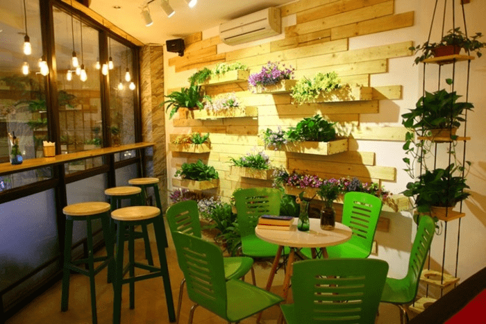 Mẫu quán cà phê đẹp sử dụng hoa, đèn và vách kính để làm sang trọng, nới rộng không gian.